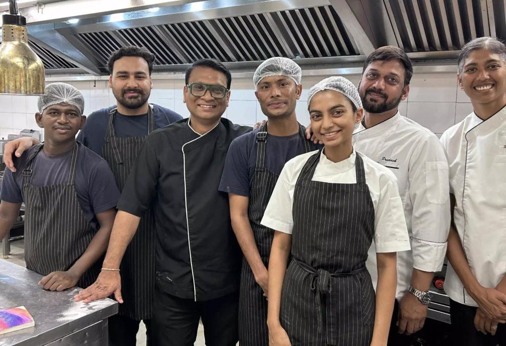 A group of kitchen staff and chefs smiling together in a commercial kitchen.