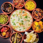 South Indian meal with rice surrounded by assorted vegetable curries, chutneys, pickles, and papad served in clay pots.