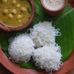 Traditional South Indian idiyappam served with chickpea curry and tea on a banana leaf.