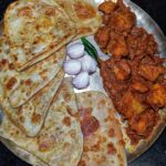 Parotta served with spicy chicken curry, onions, and a green chili on a plate.