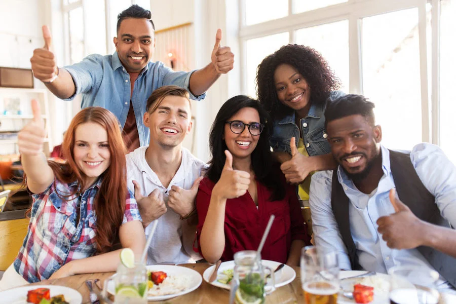 A group of happy friends giving thumbs up at a restaurant table.