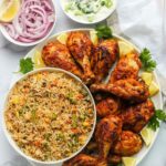 “Grilled chicken drumsticks served with vegetable rice and raita in a Bangalore restaurant”