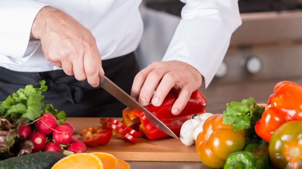 Chef washing fresh vegetables in a sanitized restaurant kitchen to ensure hygienic handling from start to finish.